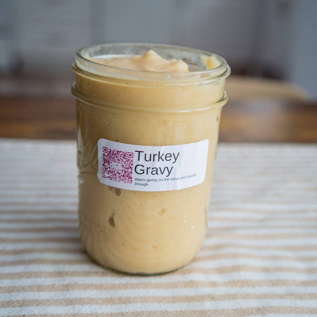 Jar of turkey gravy on a striped tablecloth with a blurred background